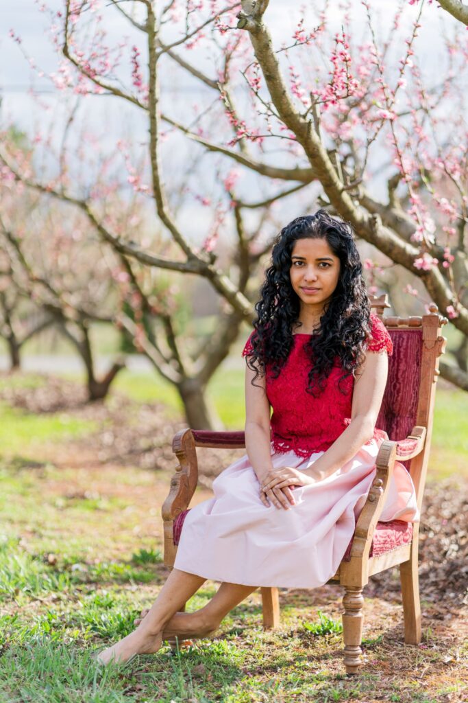 Model Minnie sits in a red chair beneath peach blossoms in Charlotte NC