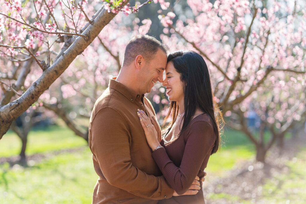 Smiling couple touching foreheads in a peach blossom orchard in Charlotte NC