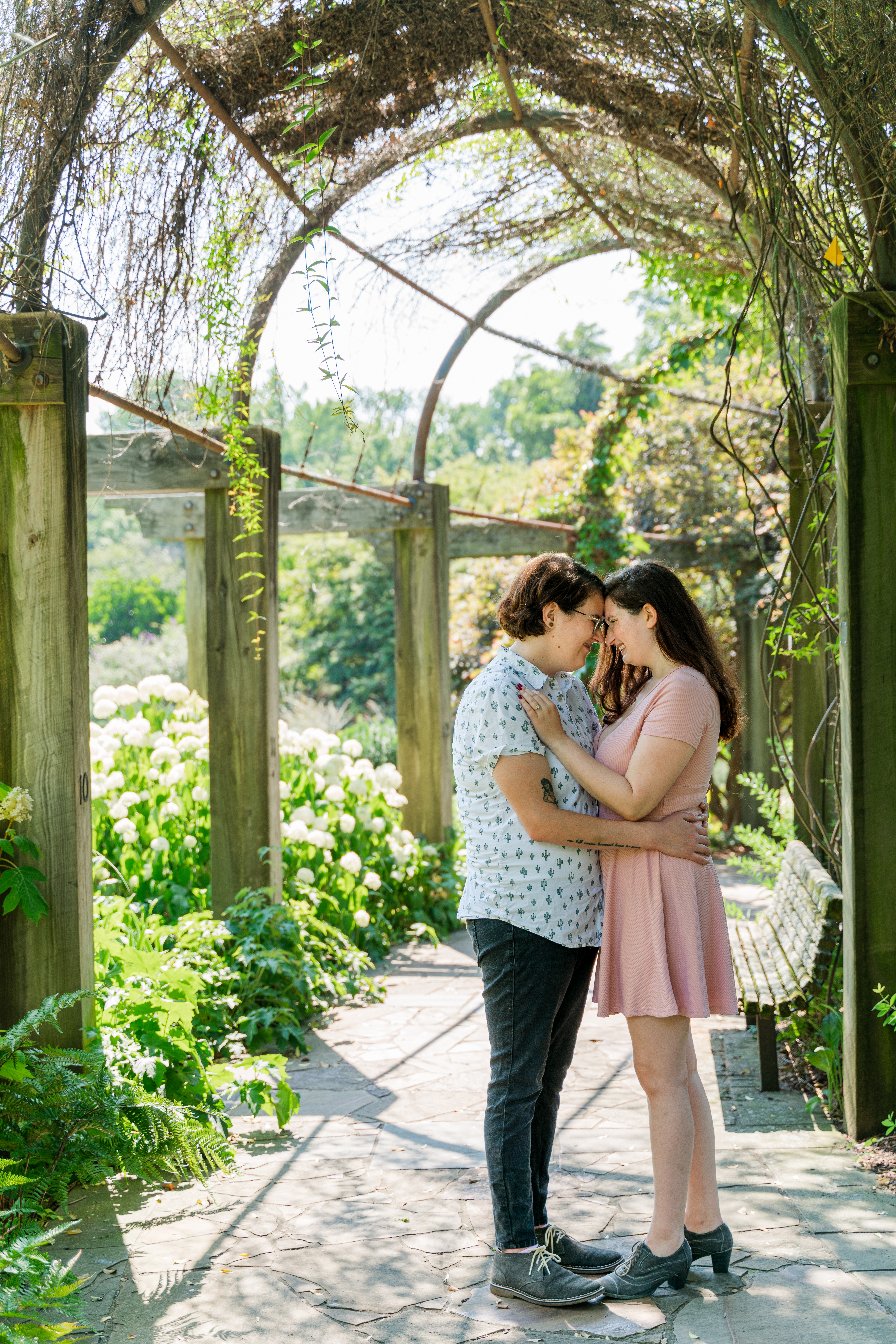 Kayla and Jax pose under Greensboro Arboretum's arch, surrounded by white hydrangeas.