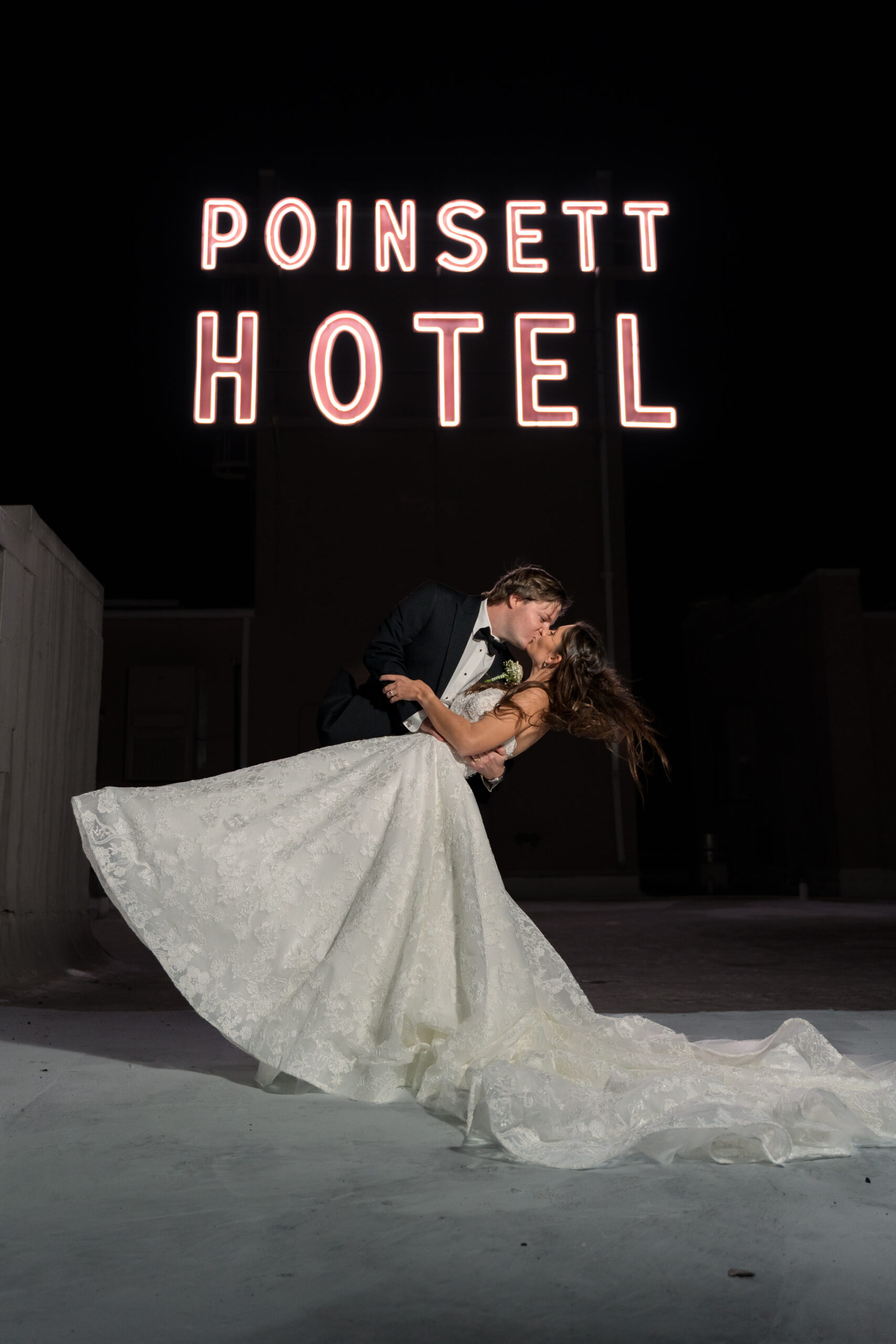 Anna and Sam share a kiss and a dip at night on the top of the Westin Poinsett. A huge, read, neon sign reading "Poinsett Hotel" shines behind them in the dark.