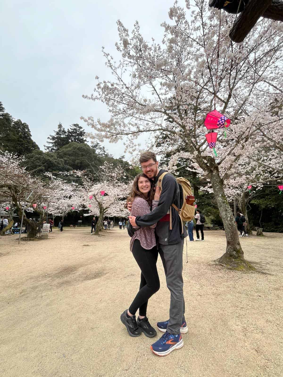 Katie Lumsden, the owner of The Lilac Lion Photography poses with her husband under the Japanese cherry blossoms in full bloom in Hiroshima, Japan.