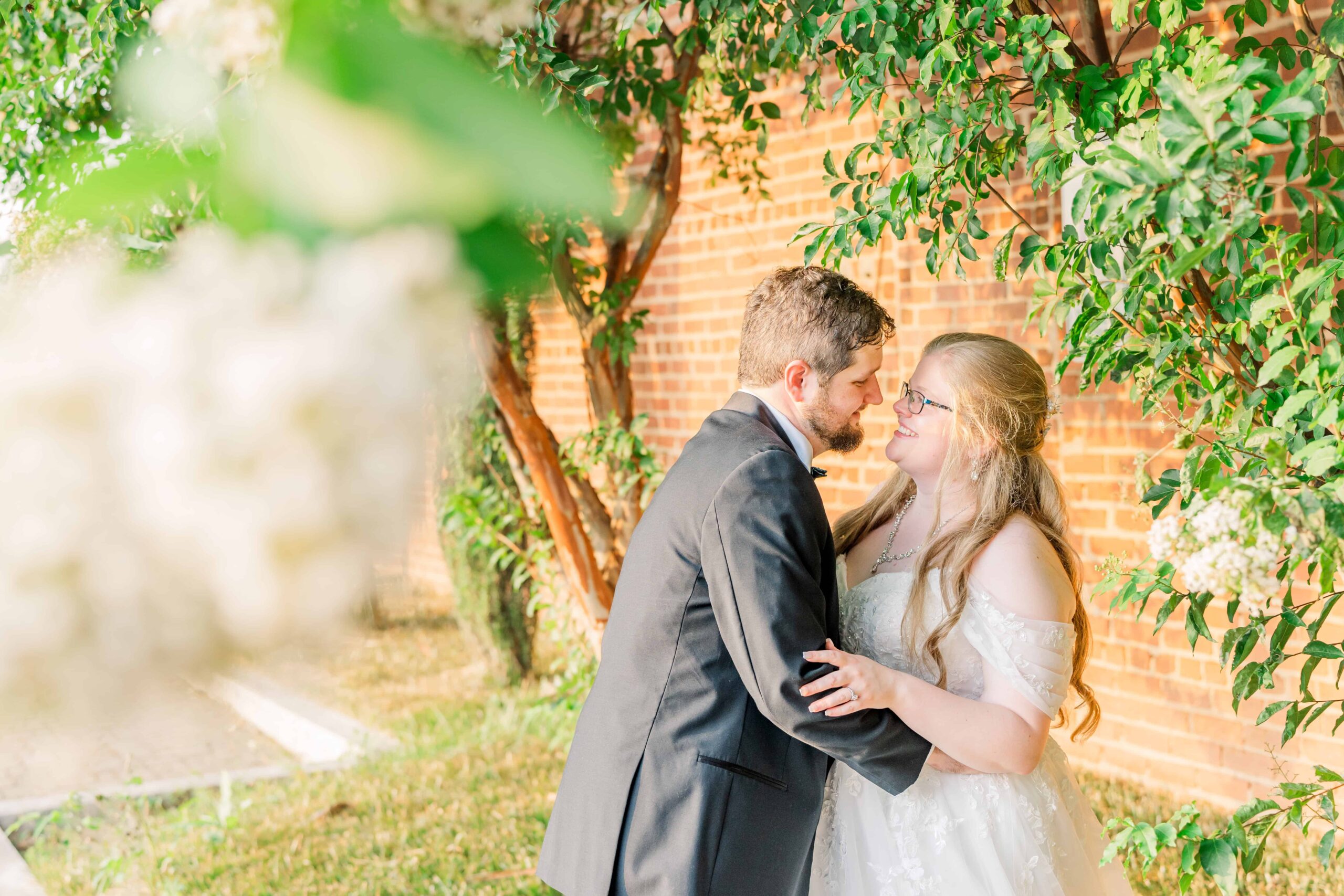 Eric and Erica pose under a blooming, white crepe myrtle tree during their wedding day at warehouse 18 venue in Hickory, NC.