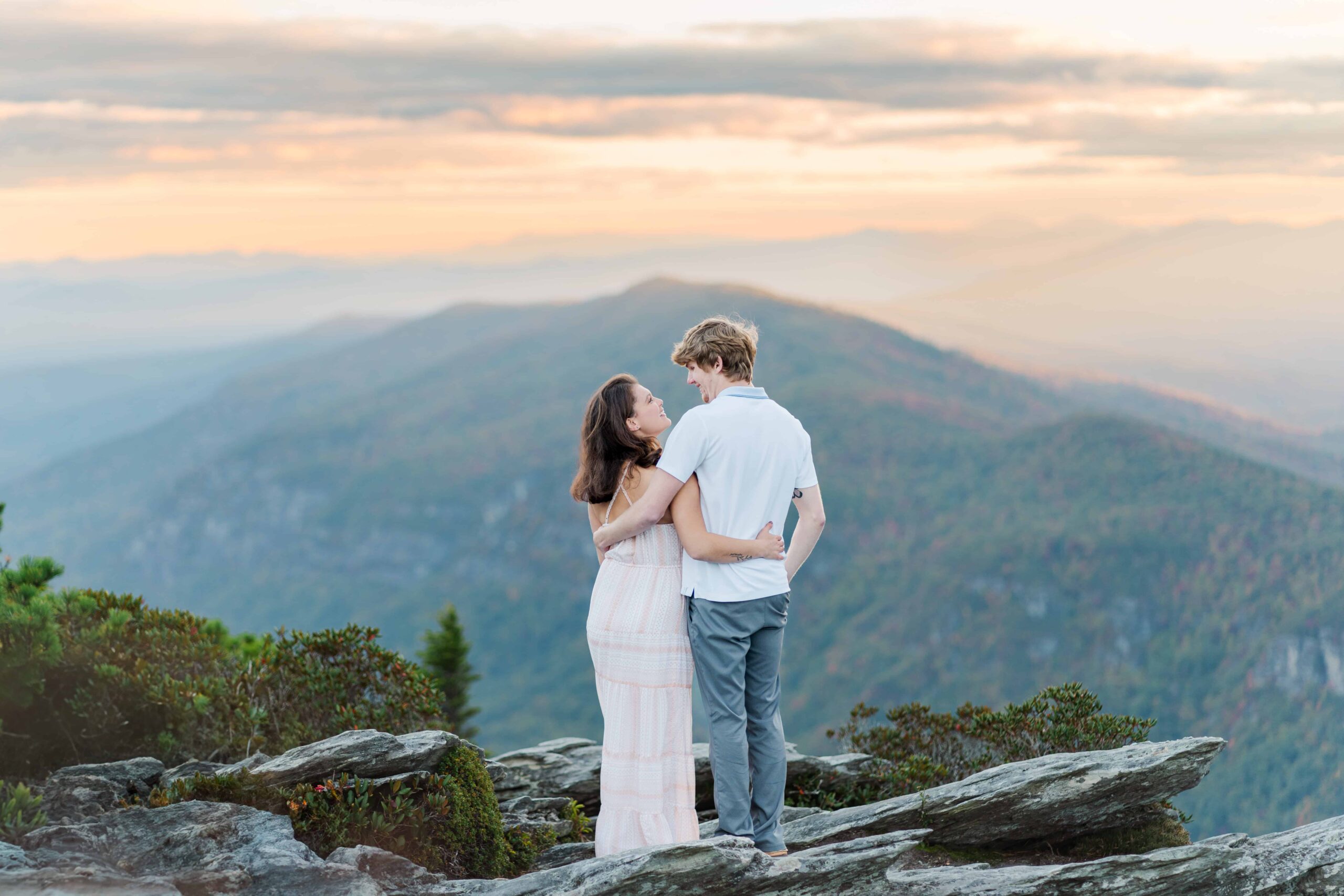 Couple holding hands on Hawksbill Mountain summit at sunset, surrounded by vibrant fall foliage in the Blue Ridge Mountains.