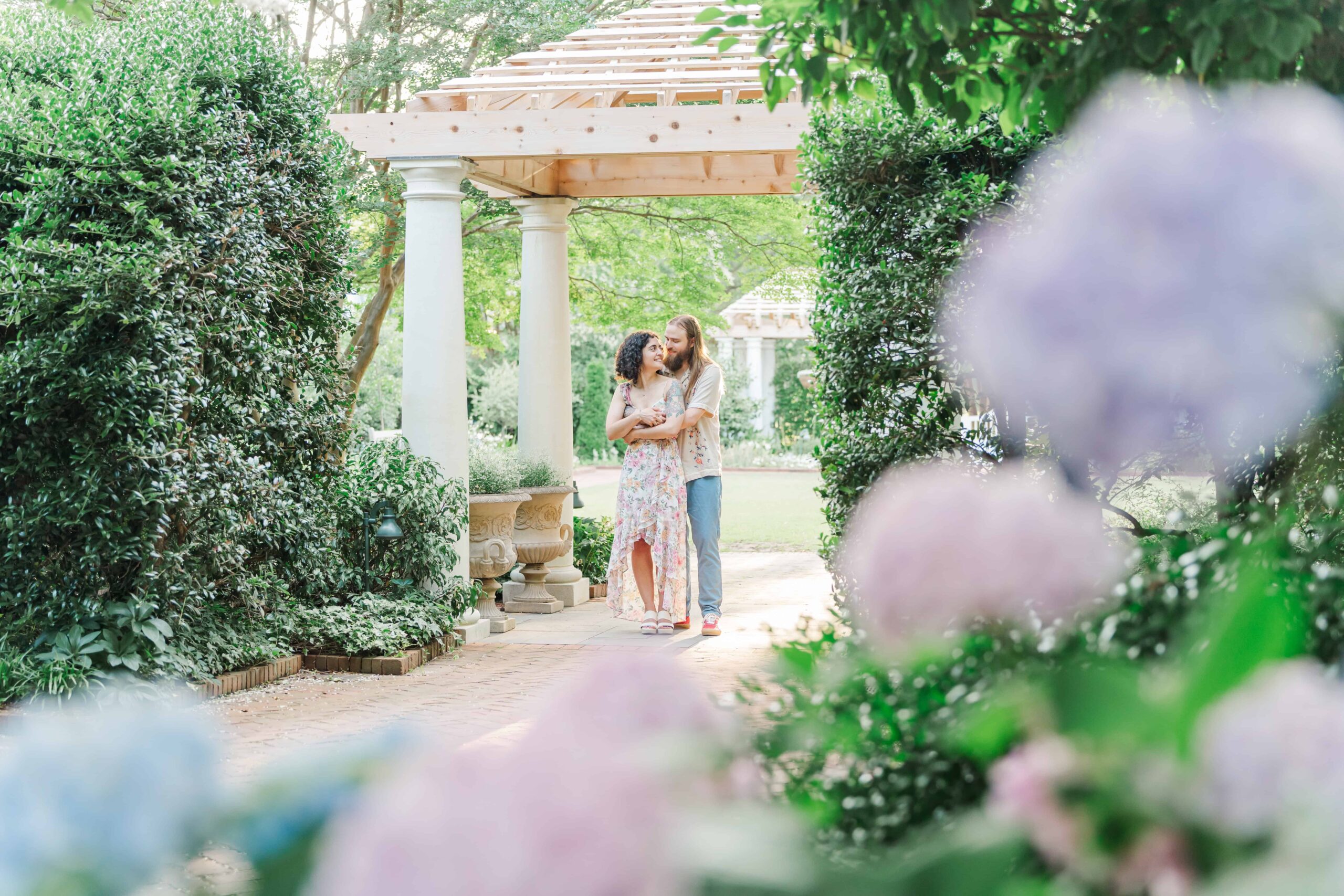 Engaged couple posing in the White Garden at Daniel Stowe Botanical Gardens with blooming hydrangeas