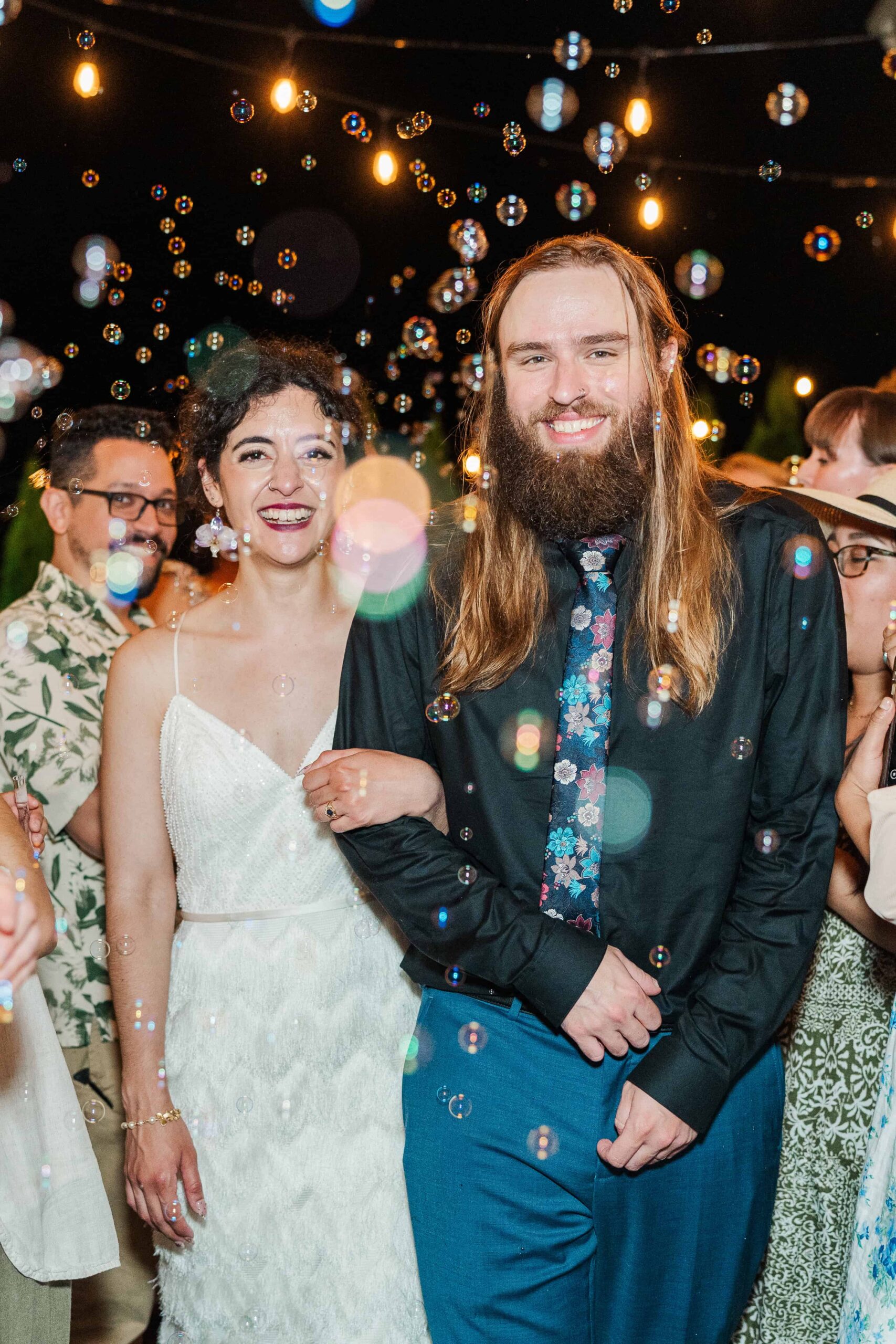 Bride and groom bubble exit in the rain under string lights