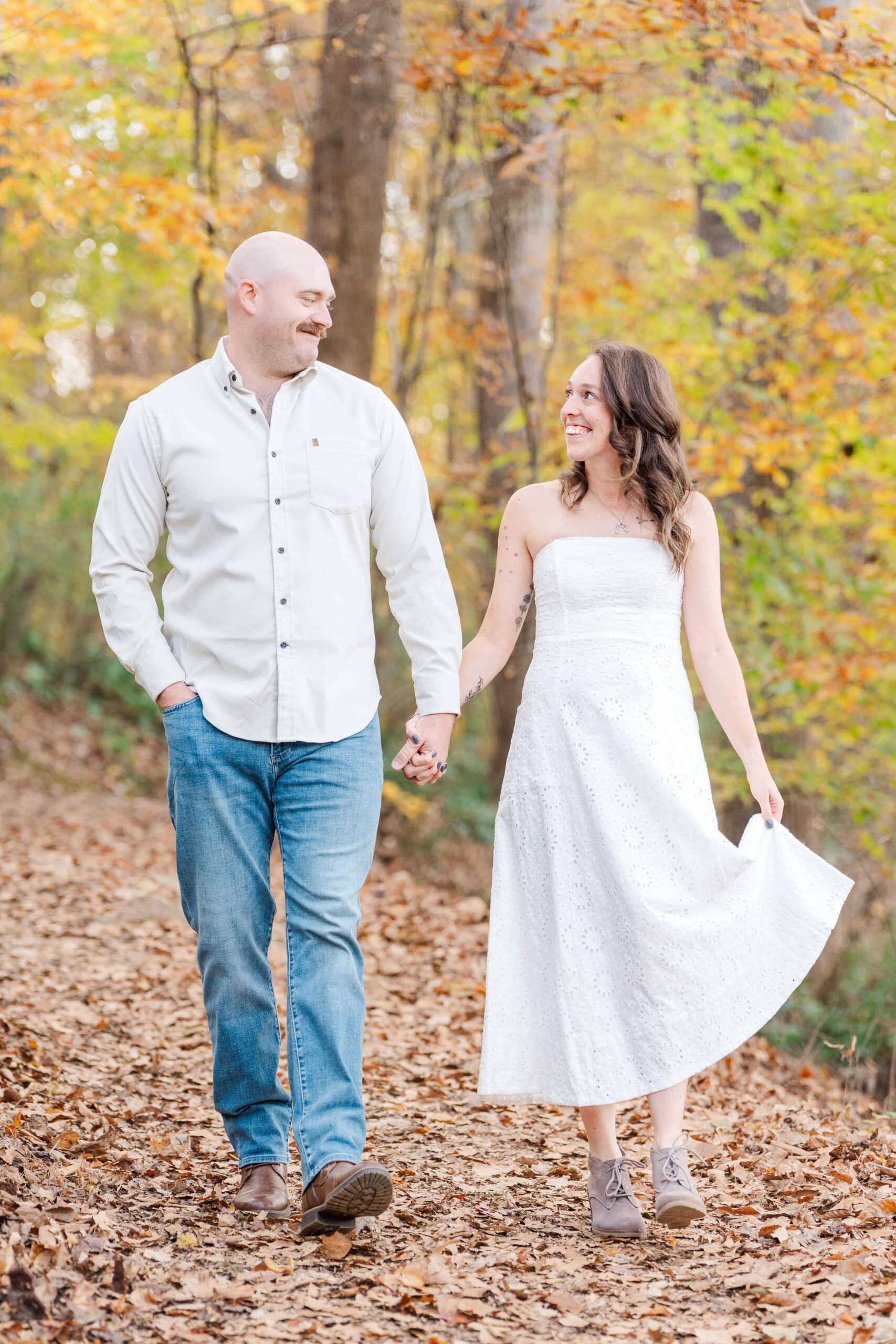 Couple holding hands on wooded trail surrounded by natural scenery