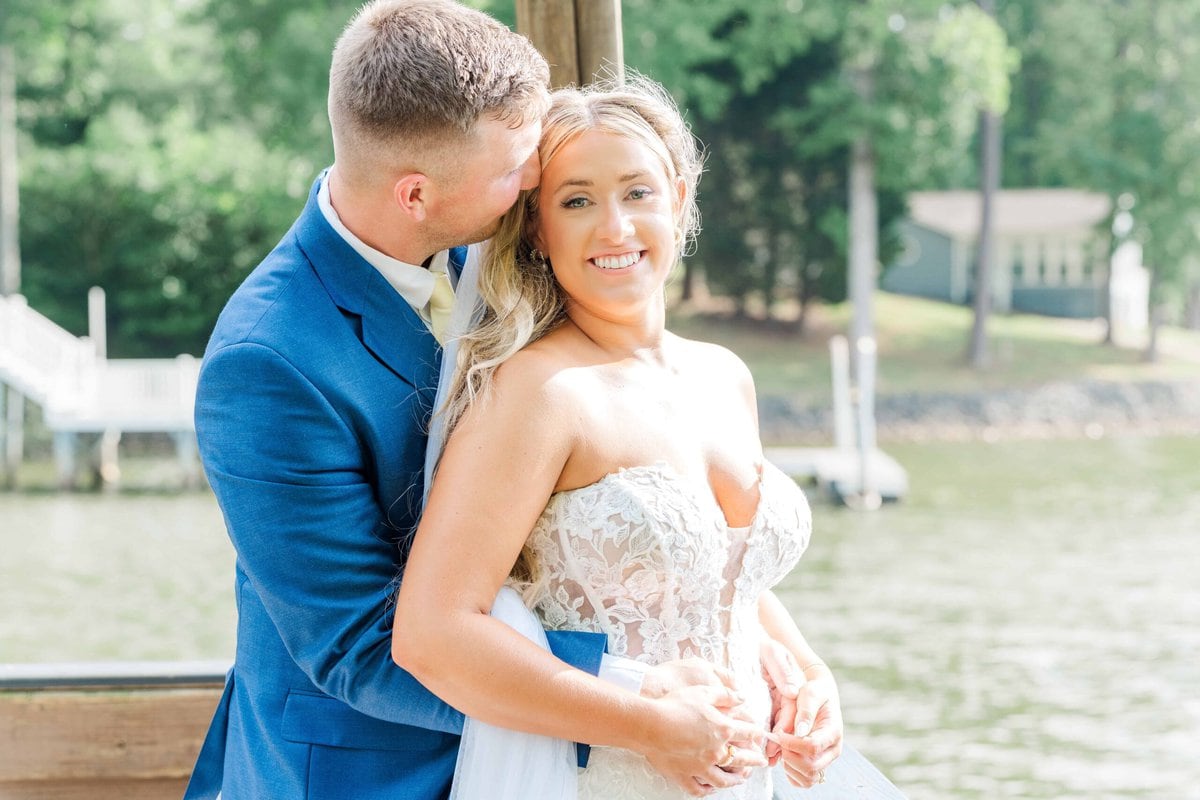 Bride and groom embracing by the waterfront location at Camelot Meadows